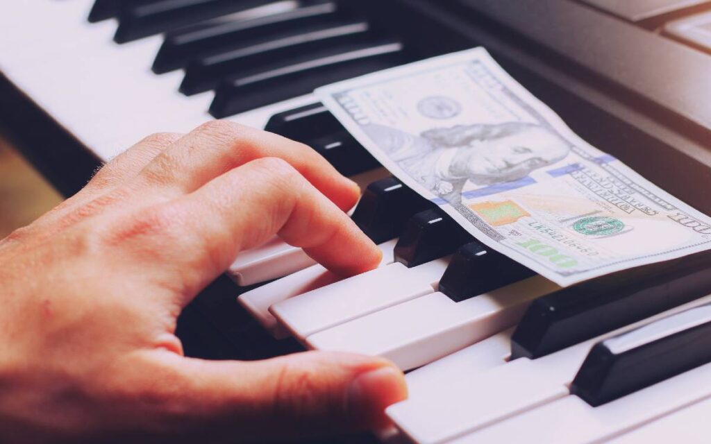 $100 bill on piano keys and musician's hand
