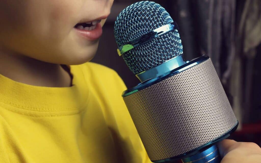 Child in a yellow t-shirt holding a microphone singing a song