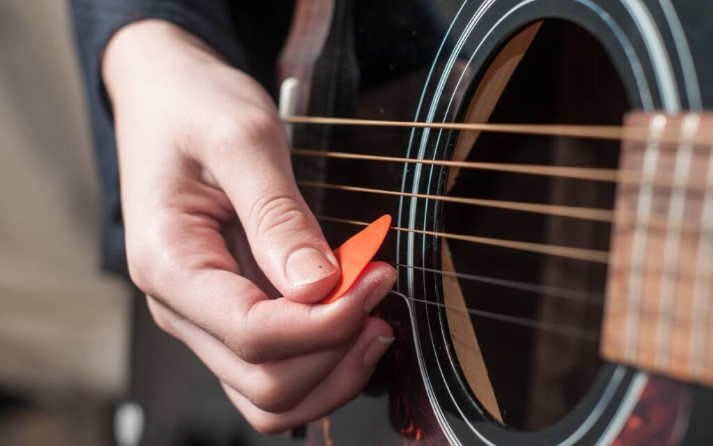Female hand strumming an acoustic guitar using a guitar pick