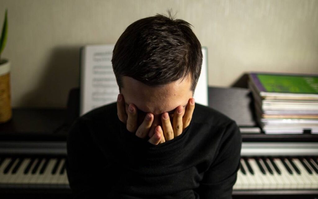 Frustrated pianist man sitting with his back to the piano putting his face in his hands
