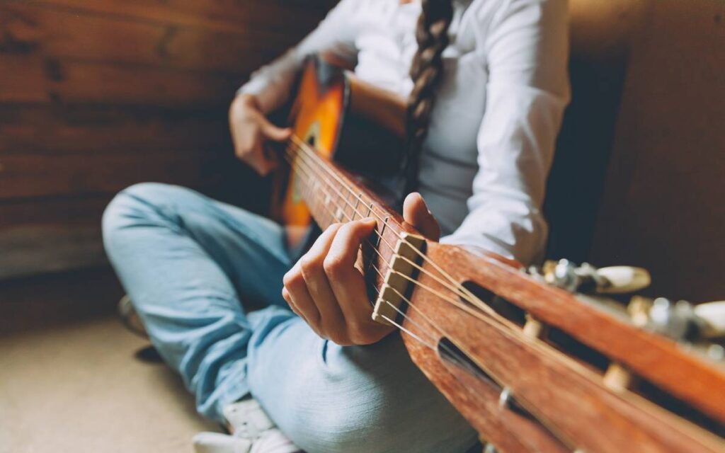 Girl sitting comfortably in the corner of her room playing an acoustic guitar