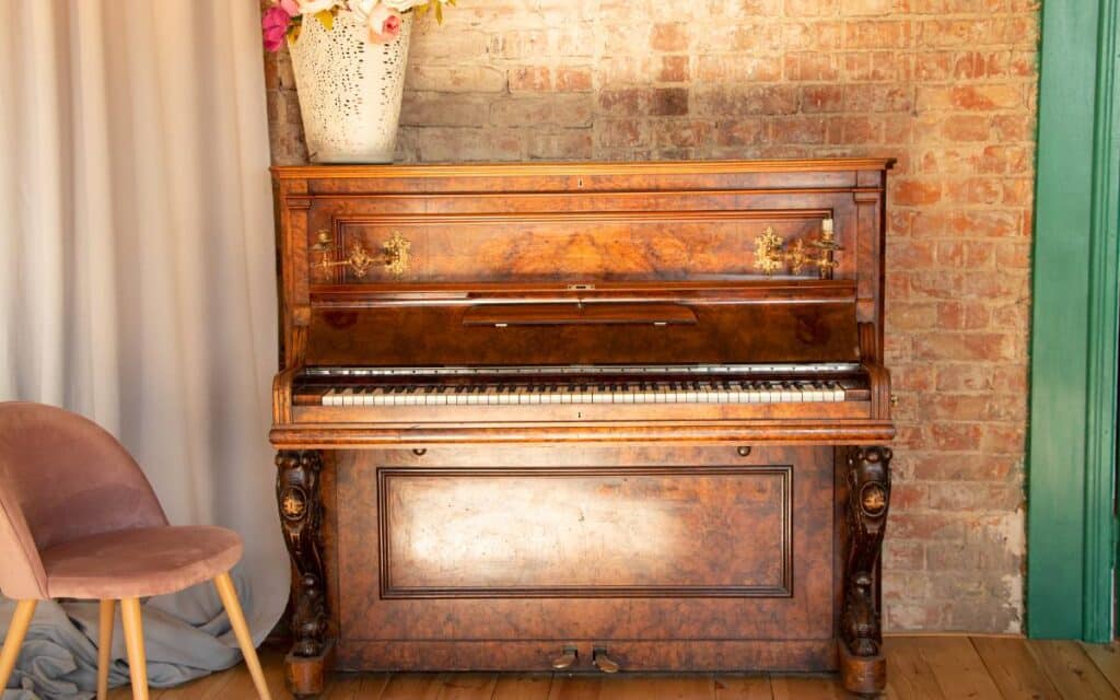 Old brown piano in a room illuminated by sunlight against a brick wall