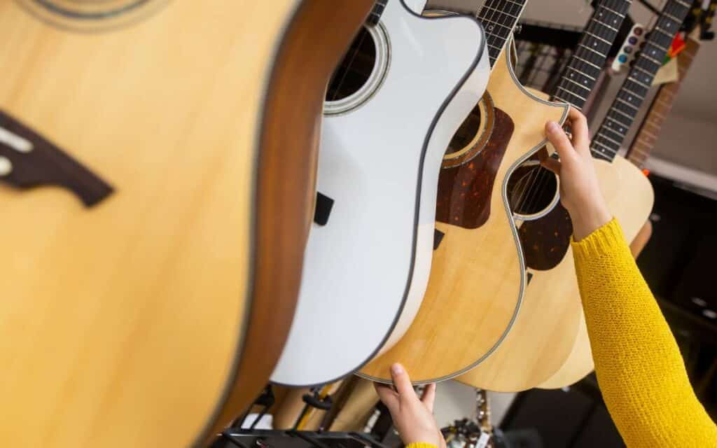 Rows of guitars in a guitar shop, view of a woman's hand selecting an acoustic guitar