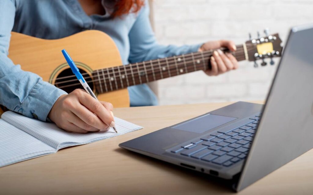 Woman with a guitar writing notes while having guitar lessons online