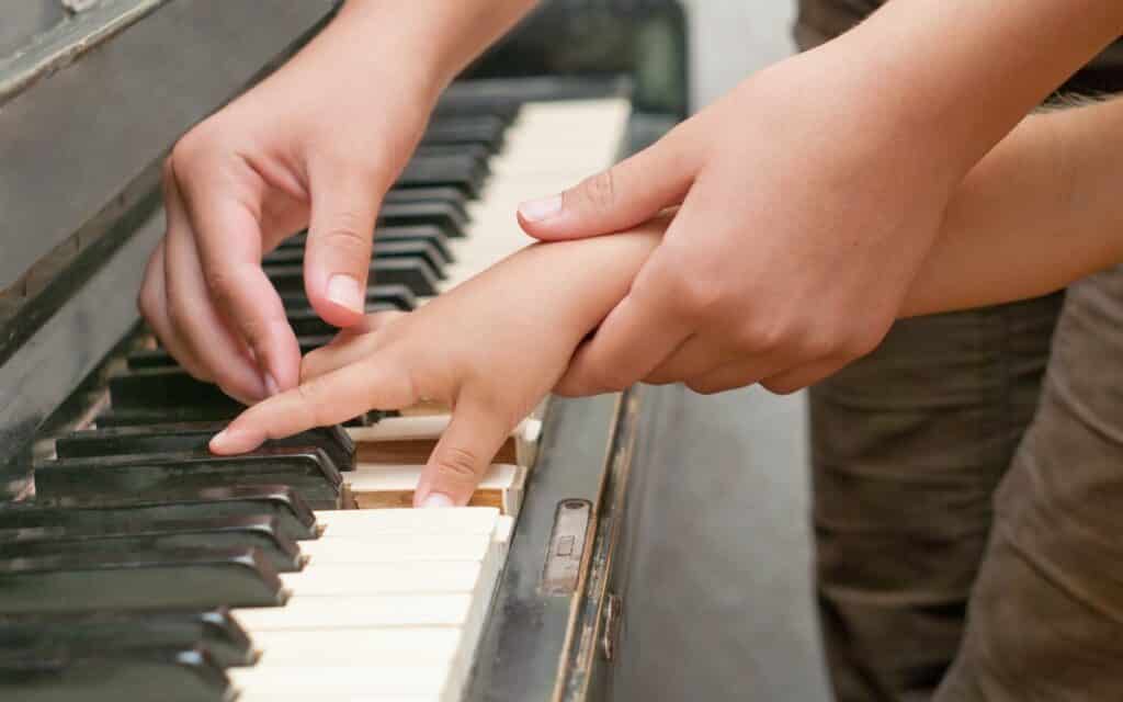 Hands of a piano teacher helping a young student play the piano