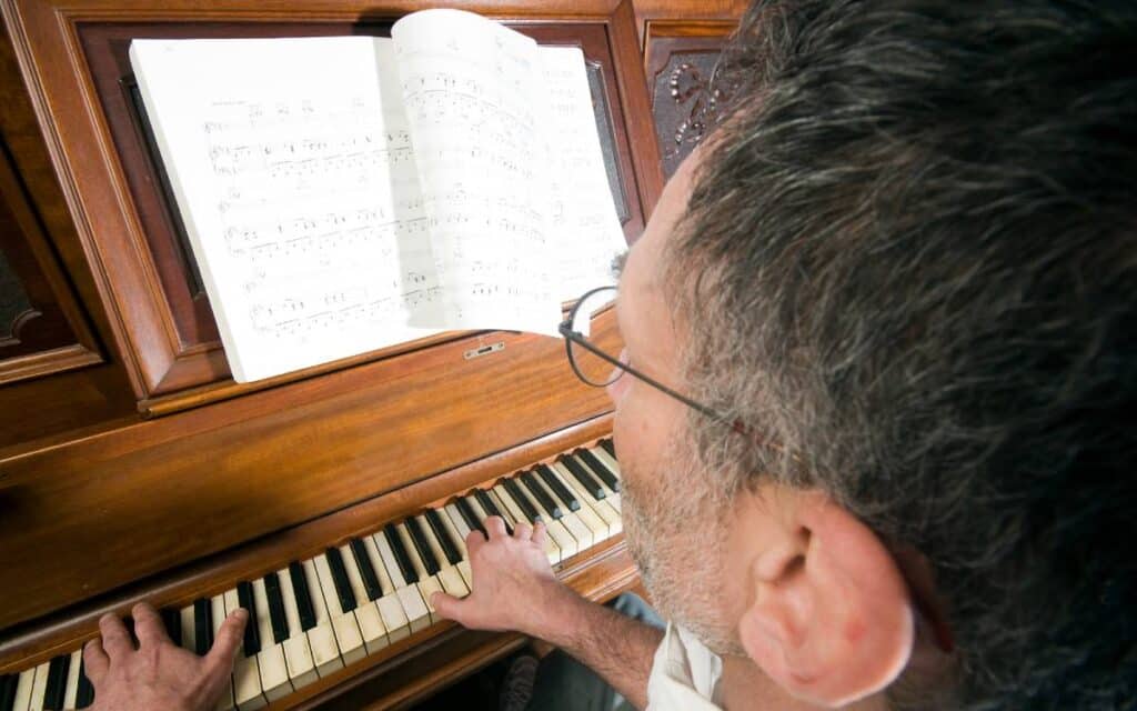 Middle-aged man with glasses reading music sheet and playing the piano