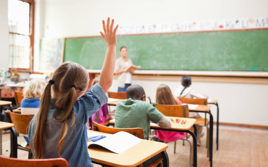 Back view of elementary girl student raising her hand in class