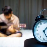 Alarm clock on bedside table with blurry background of a boy playing guitar on his bed