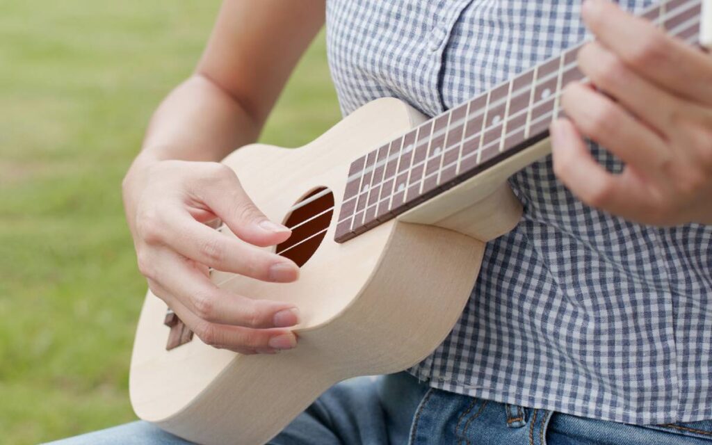 Close up of a woman sitting on the grass and playing ukulele