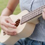 Close up of a woman sitting on the grass and playing ukulele