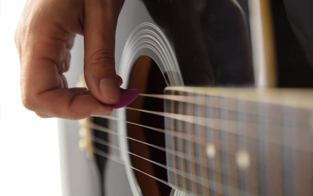 Close up of hand strumming acoustic guitar using a guitar pick