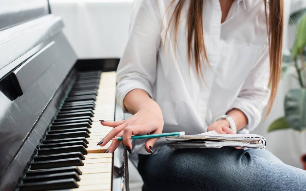 Girl in white shirt with notebook playing piano and composing music