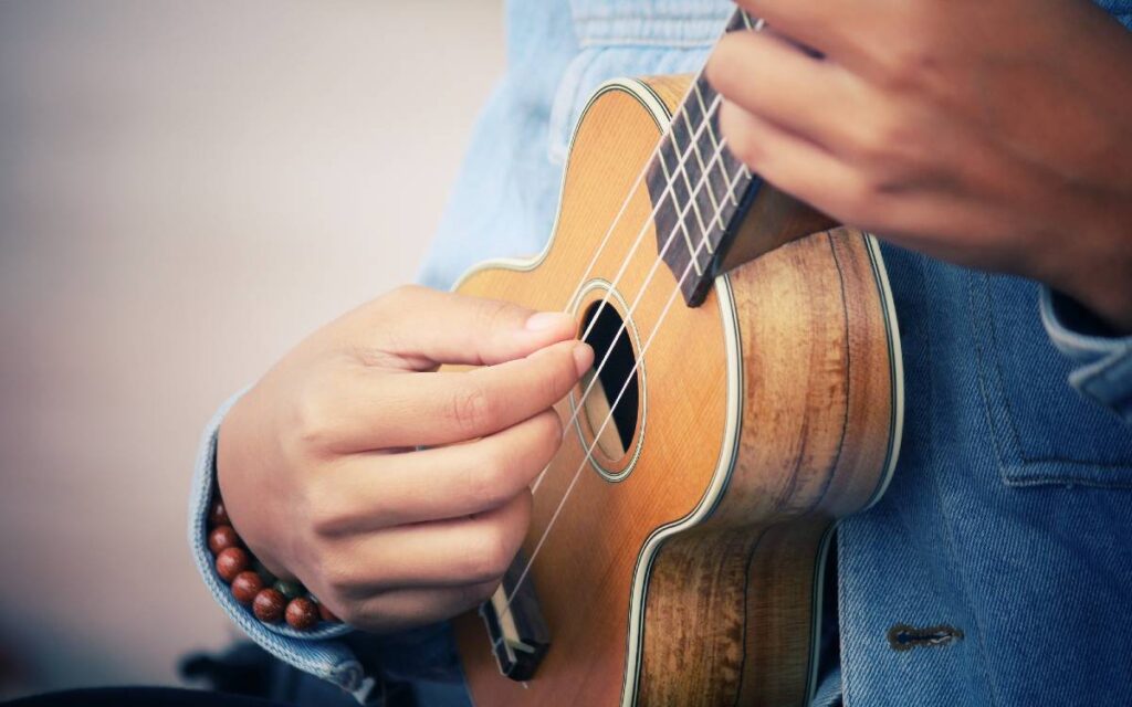 Hands of man holding and playing ukulele