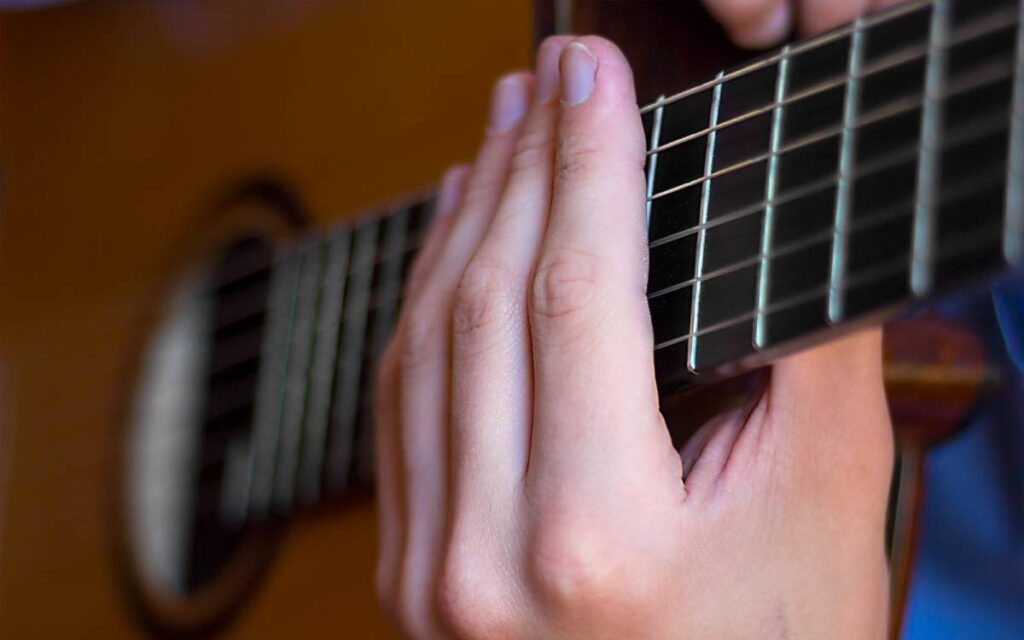 Male's hand on acoustic guitar fretboard