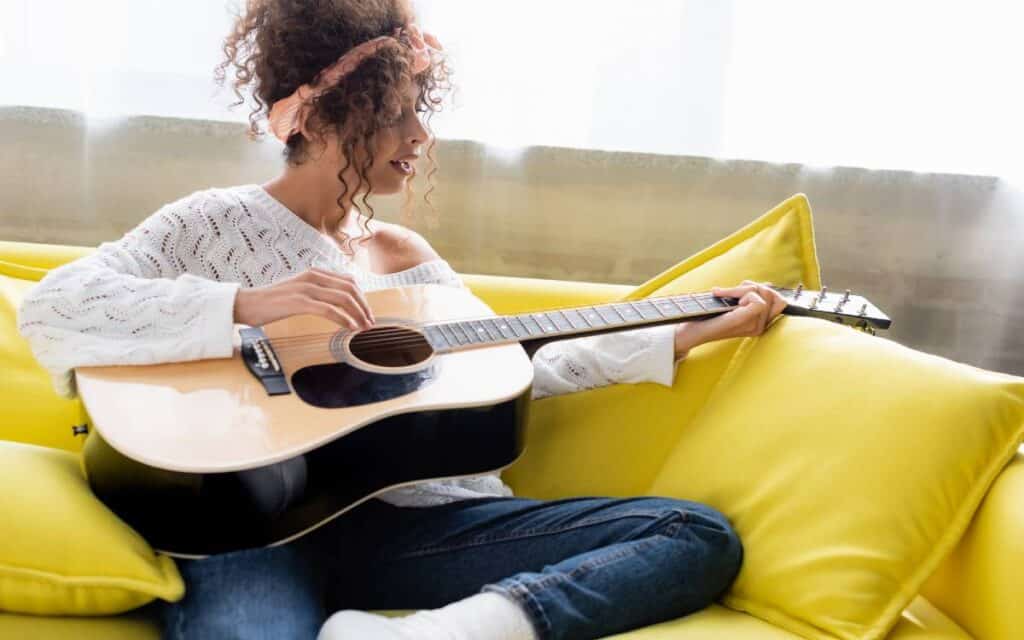 Woman with curly hair playing acoustic guitar in the living room