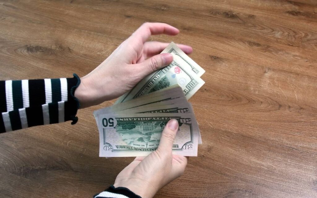 Woman's hands counting dollar bills on wooden table