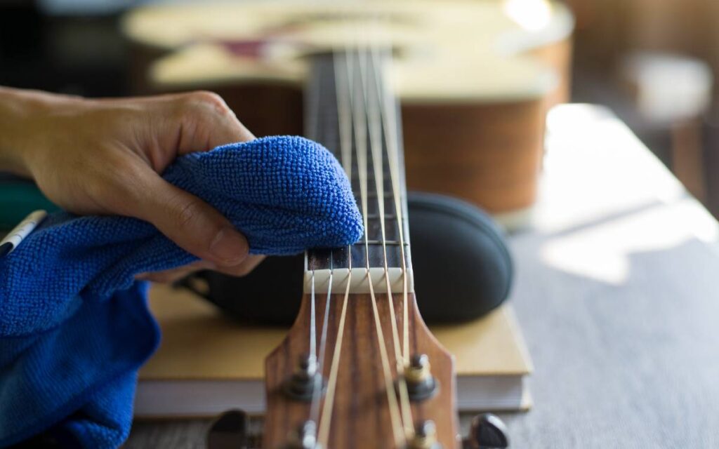 A man's hand cleaning acoustic guitar strings using a blue cloth