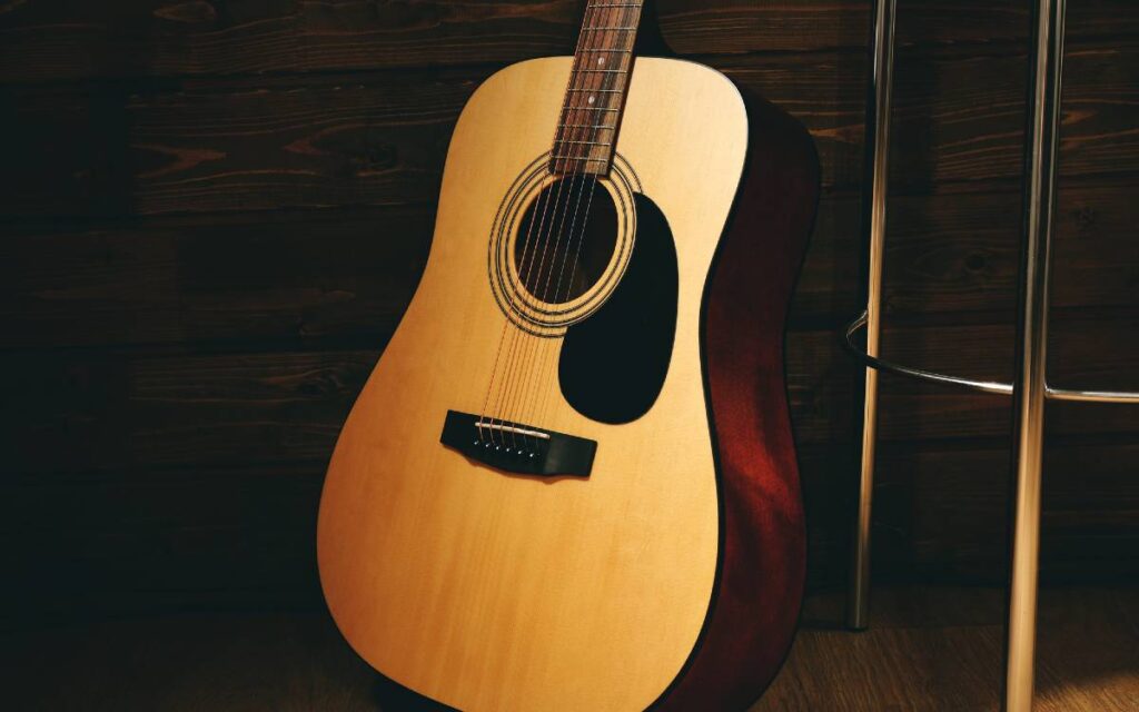 Acoustic guitar propped on wooden wall next to a bar stool
