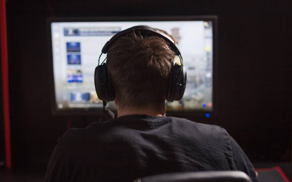 Back view of a man wearing headphones playing a game on his computer