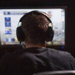 Back view of a man wearing headphones playing a game on his computer