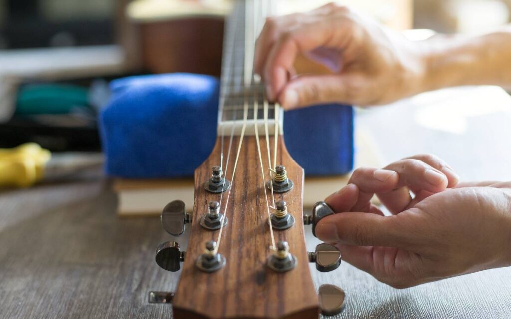 Close up of hands holding and turning tuning pegs of an acoustic guitar