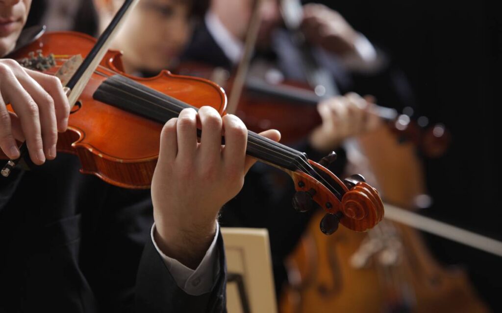 Close up of man playing the violin with blurred woman and man playing the violin and cello in the background