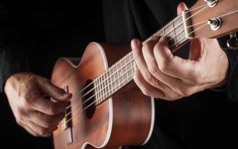 Easy beatles ukulele songs_man's hands playing ukulele on black background