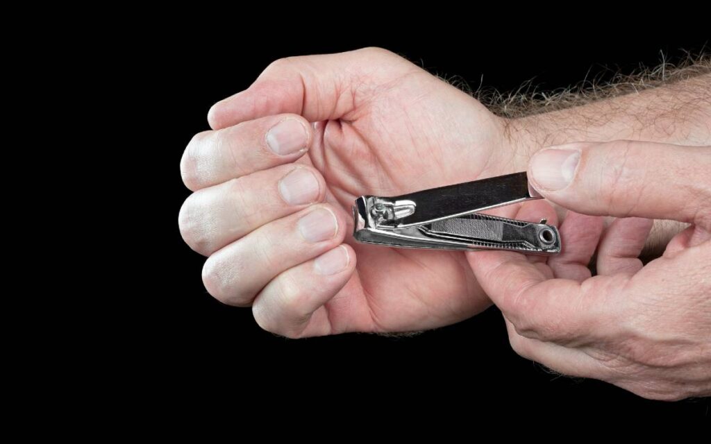 Hands of a man trimming his fingernails on black background