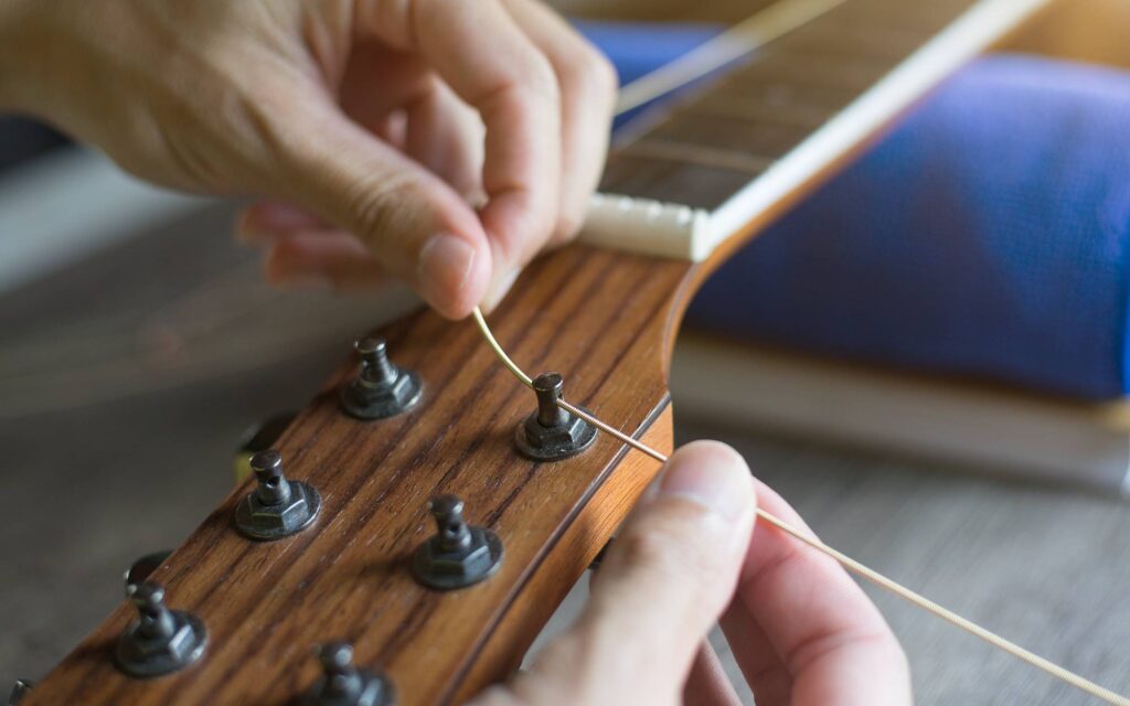 Hands of a man inserting a new string in an acoustic guitar's tuning peg