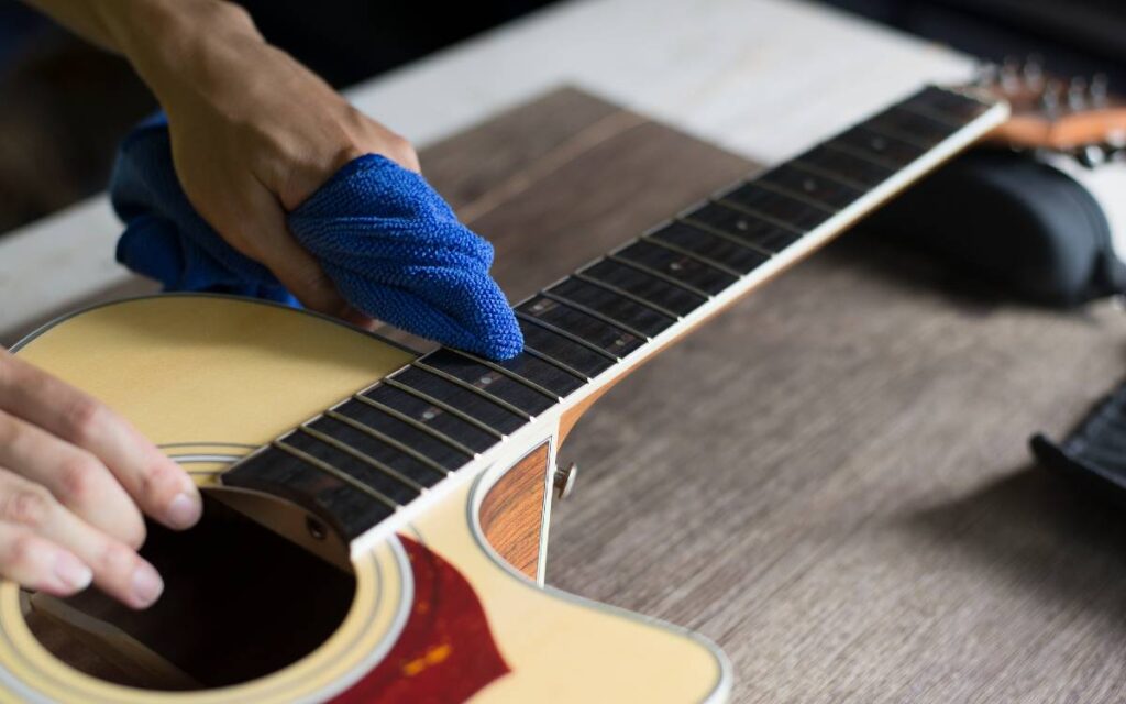 Male hands cleaning an acoustic guitar's fretboard