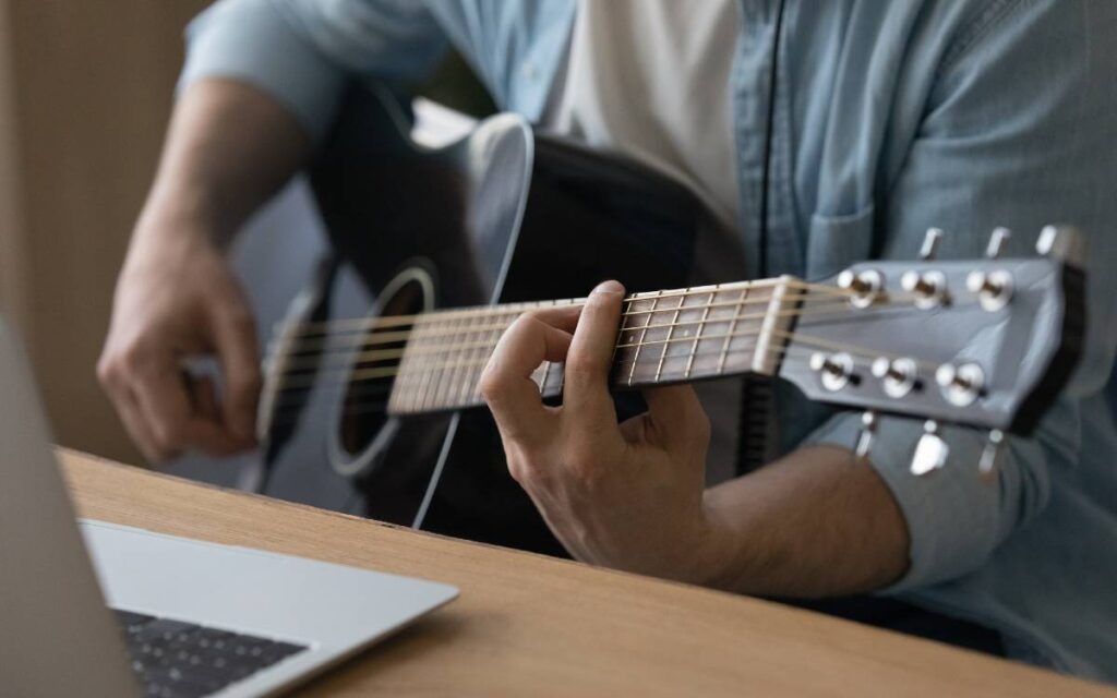 Man in front of his laptop playing the guitar