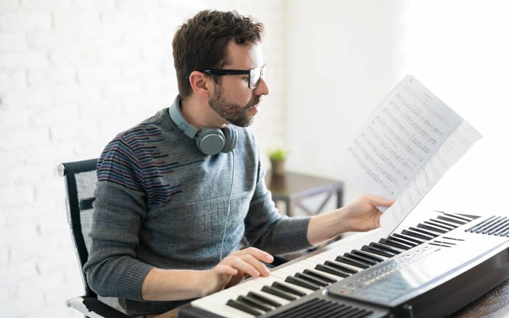 Man reading and holding music sheet while one hand on piano keys
