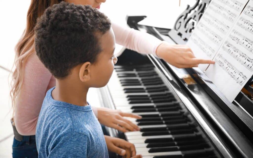 Piano teacher teaching little boy to read sheet music