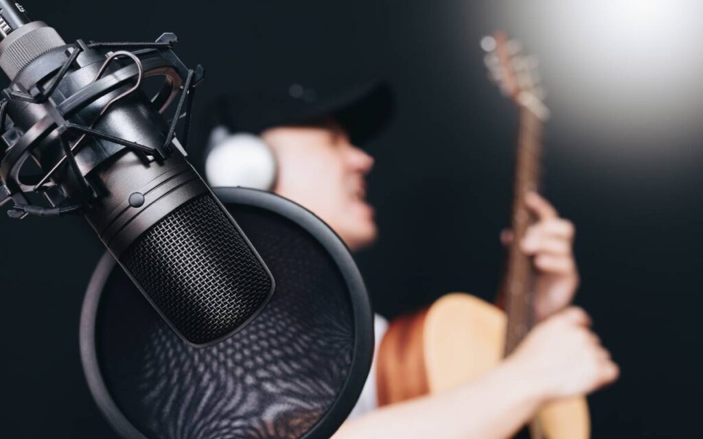 Close up of a condenser microphone with blurred man singing and playing the guitar in the background