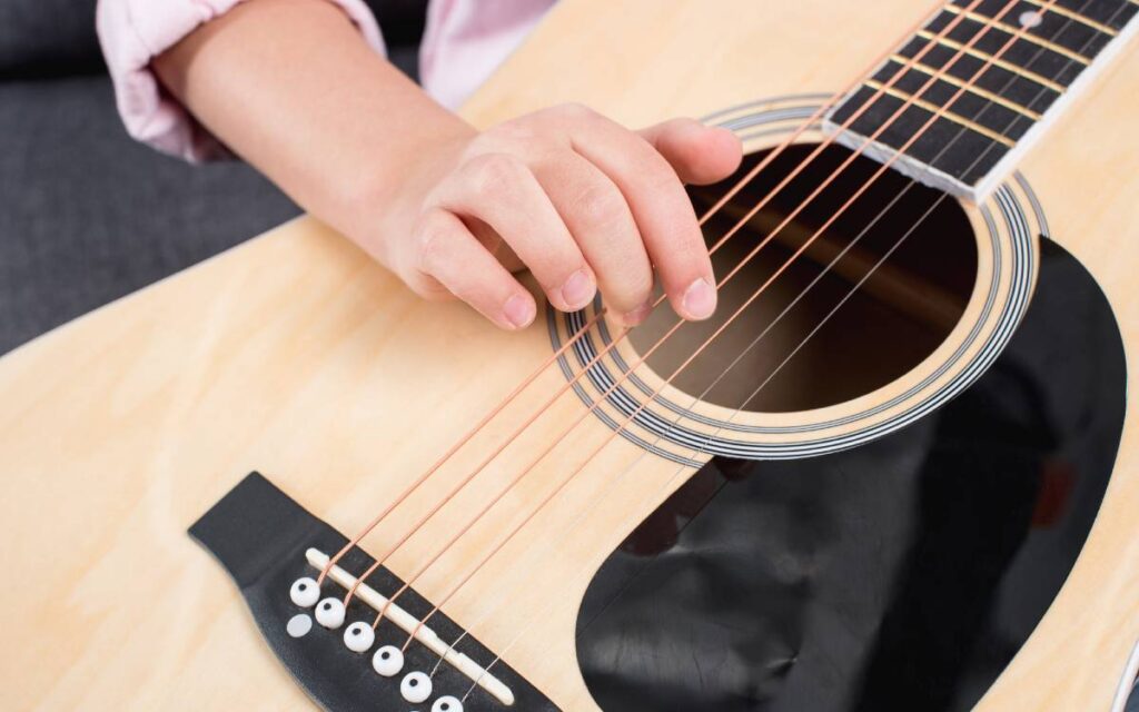 A kid's hand strumming an acoustic guitar