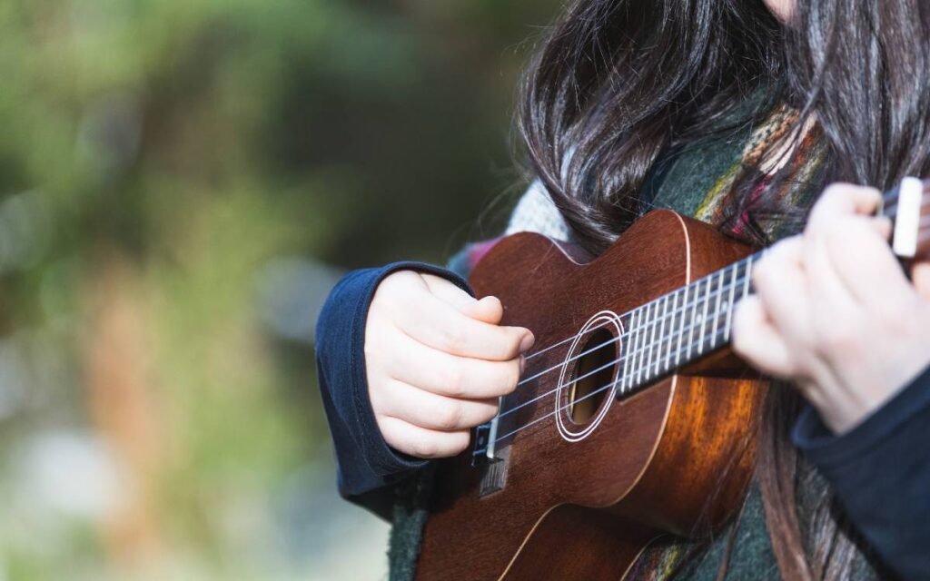 Young woman with long hair playing ukulele outdoors