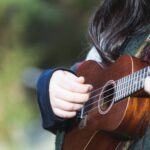 Young woman with long hair playing ukulele outdoors