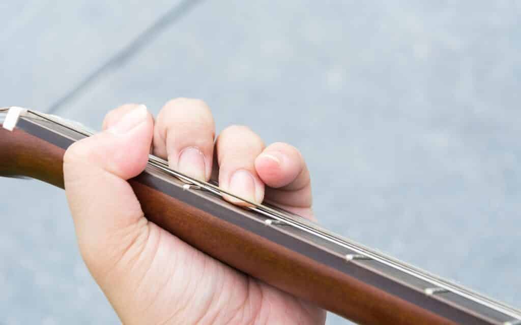 Acoustic guitar neck closeup with man's hand holding a chord