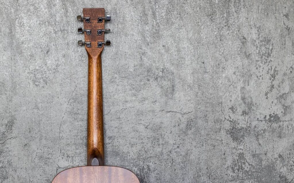 Back view of acoustic guitar neck on concrete wall