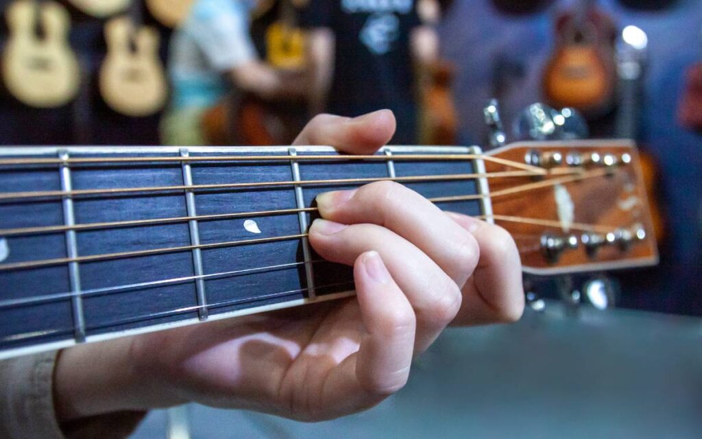 Female hand playing a chord on a wide neck acoustic guitar