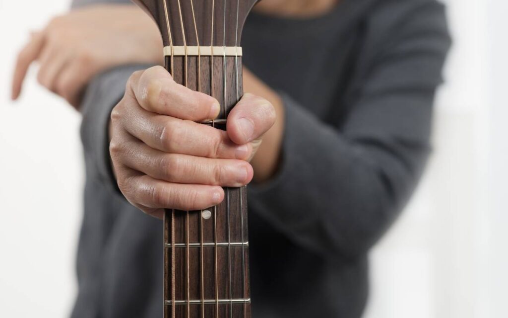 Man holding an acoustic guitar by the neck