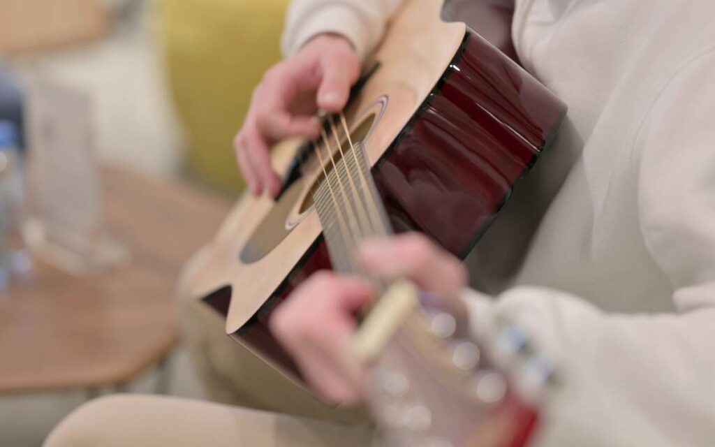 Man playing acoustic guitar and contemplating the question is electric guitar easier than acoustic guitar