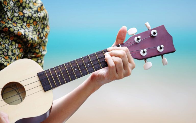 Cropped photo of a man in hawaiian shirt playing ukulele at the beach