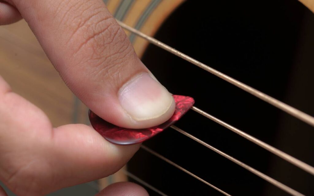 Closeup of a man's hand holding a guitar pick, strumming an acoustic guitar's string