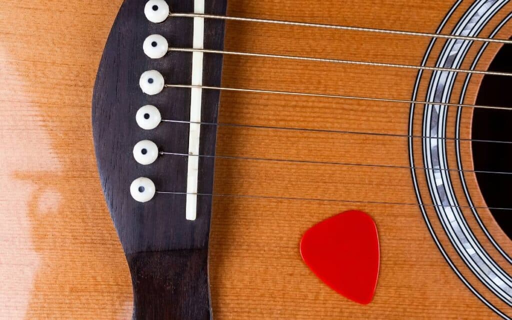 Red guitar pick on an acoustic guitar