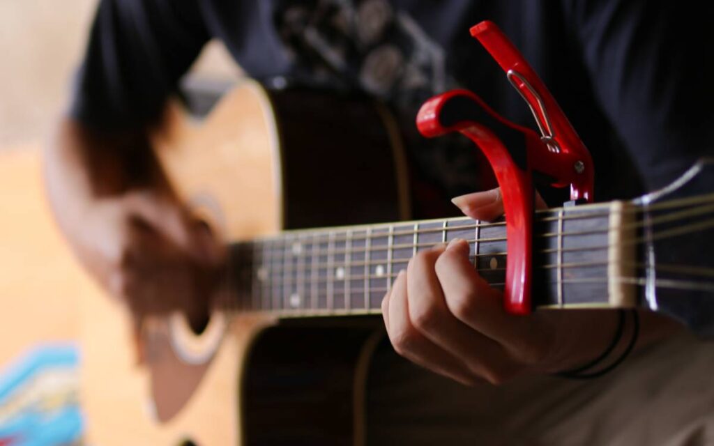 Man playing acoustic guitar with red guitar capo