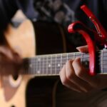 Man playing acoustic guitar with red guitar capo